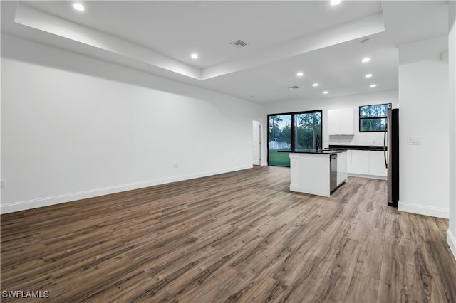 kitchen with a center island, light wood-type flooring, a tray ceiling, white cabinetry, and stainless steel refrigerator