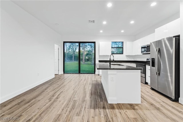 kitchen with a sink, white cabinets, appliances with stainless steel finishes, light wood finished floors, and dark countertops