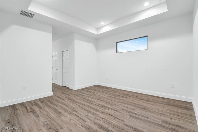 empty room with recessed lighting, a raised ceiling, visible vents, wood finished floors, and baseboards