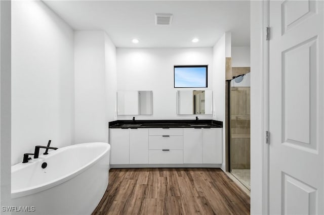 full bath featuring double vanity, visible vents, a freestanding bath, a stall shower, and a sink