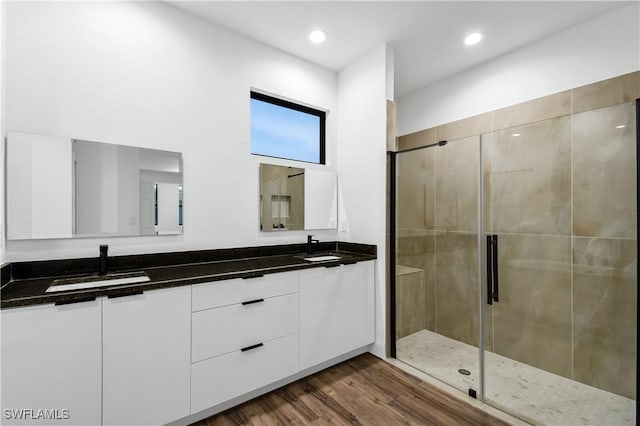 bathroom featuring double vanity, recessed lighting, a sink, a shower stall, and wood finished floors