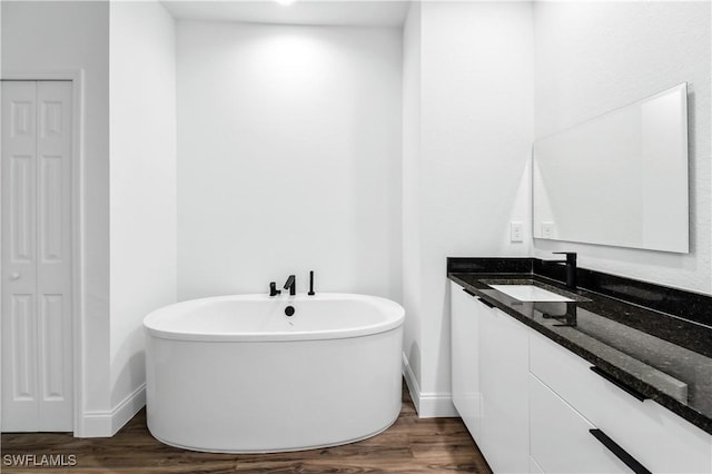 full bath with a freestanding tub, wood finished floors, vanity, baseboards, and a closet