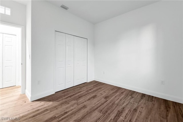 unfurnished bedroom with a closet, visible vents, baseboards, and wood finished floors