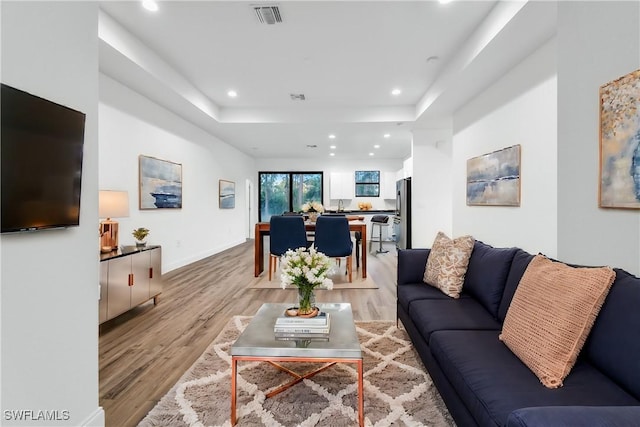 living area with light wood-style floors, recessed lighting, a raised ceiling, and visible vents