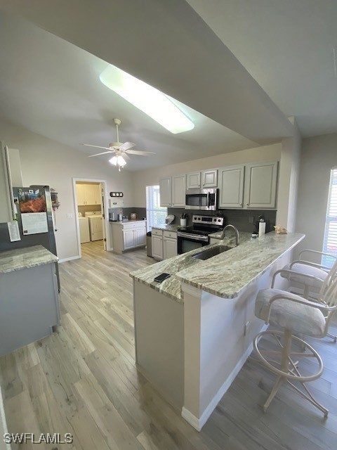 kitchen with a breakfast bar, sink, separate washer and dryer, appliances with stainless steel finishes, and kitchen peninsula