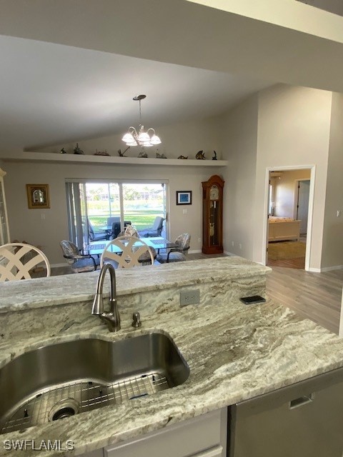 kitchen with light stone countertops, vaulted ceiling, sink, an inviting chandelier, and hanging light fixtures