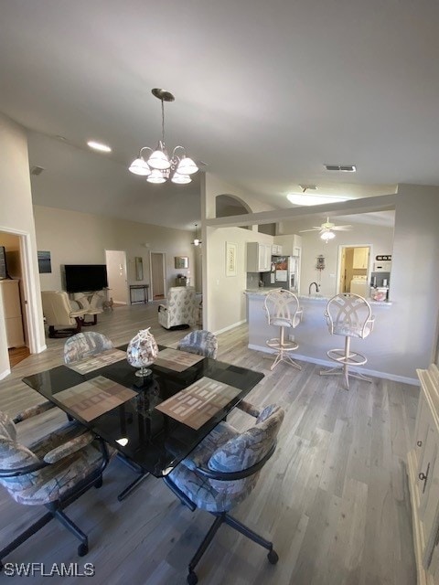 unfurnished dining area with ceiling fan with notable chandelier, light hardwood / wood-style flooring, and vaulted ceiling