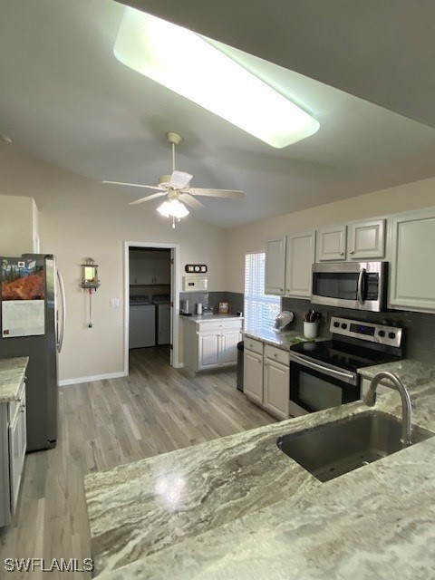 kitchen with sink, independent washer and dryer, light hardwood / wood-style floors, white cabinetry, and stainless steel appliances