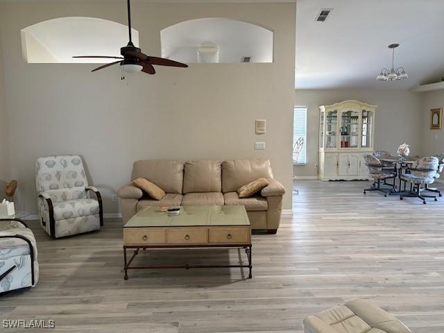 13358 Queen Palm Run, North Fort Myers, FL 33903 - living room with arched walkways, light wood-type flooring, visible vents, and ceiling fan with notable chandelier