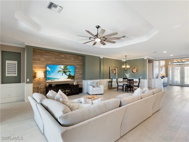 living room featuring french doors, light hardwood / wood-style flooring, a tray ceiling, ceiling fan with notable chandelier, and ornamental molding