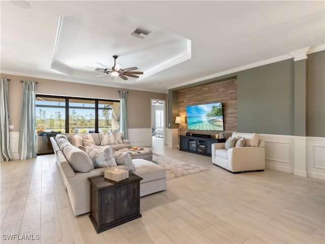 living room with ceiling fan, light hardwood / wood-style floors, a raised ceiling, and ornamental molding