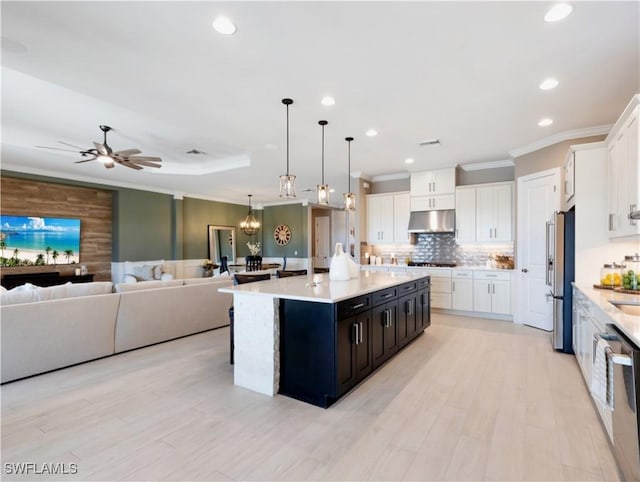 kitchen with stainless steel appliances, decorative light fixtures, white cabinets, light hardwood / wood-style floors, and an island with sink