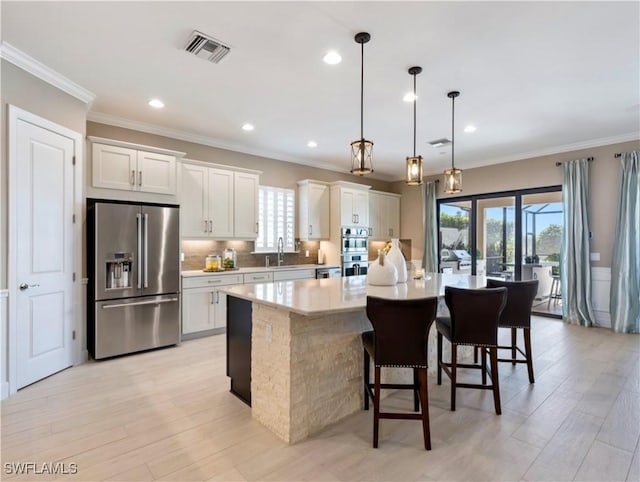 kitchen featuring white cabinetry, light hardwood / wood-style flooring, pendant lighting, a center island with sink, and appliances with stainless steel finishes