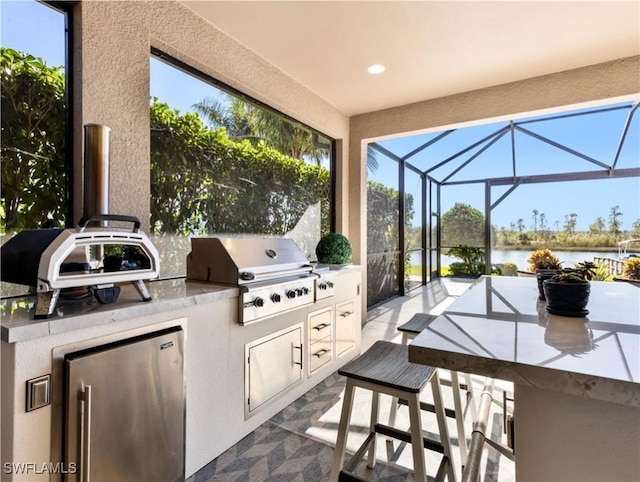 view of patio featuring glass enclosure, grilling area, an outdoor kitchen, a water view, and an outdoor bar