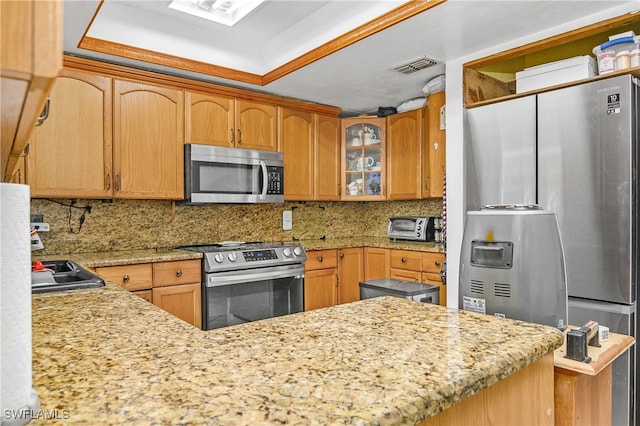 kitchen featuring kitchen peninsula, backsplash, stainless steel appliances, and a tray ceiling