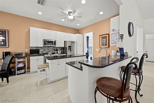 kitchen with white cabinets, a breakfast bar area, ceiling fan, kitchen peninsula, and stainless steel appliances