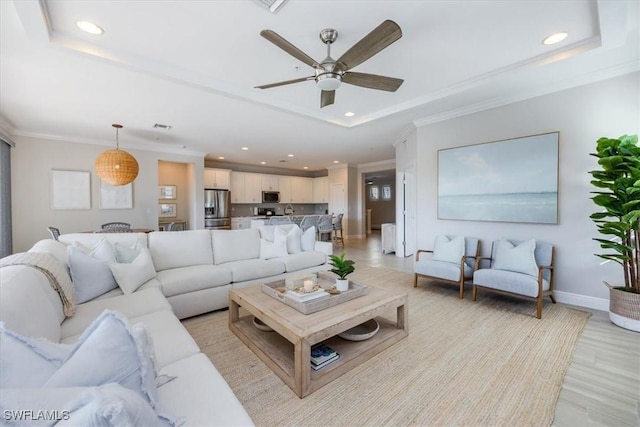 living room featuring a raised ceiling, ceiling fan, and light wood-type flooring