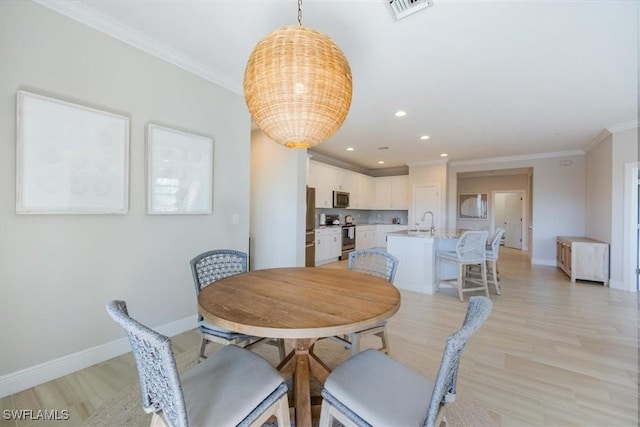 dining room featuring crown molding, sink, and light hardwood / wood-style flooring