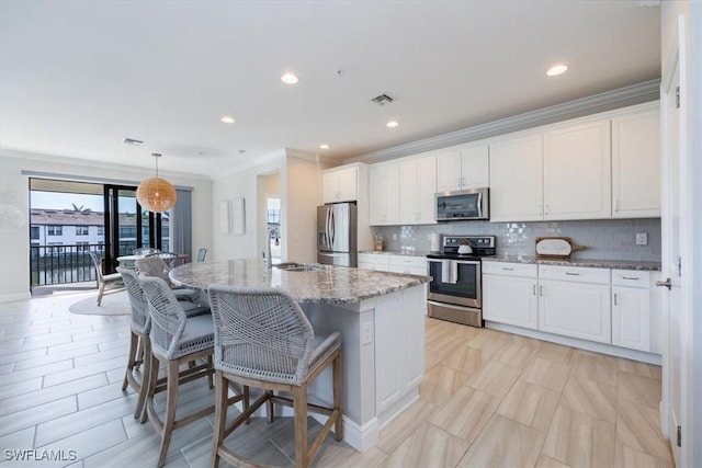 kitchen with white cabinets, a center island with sink, light stone countertops, and appliances with stainless steel finishes