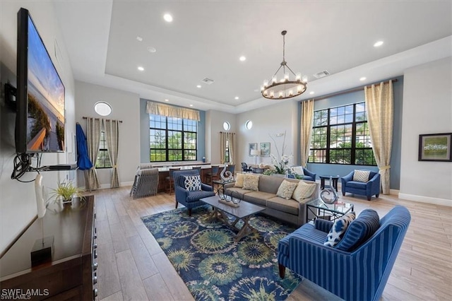 living room featuring a raised ceiling, plenty of natural light, an inviting chandelier, and light wood-type flooring