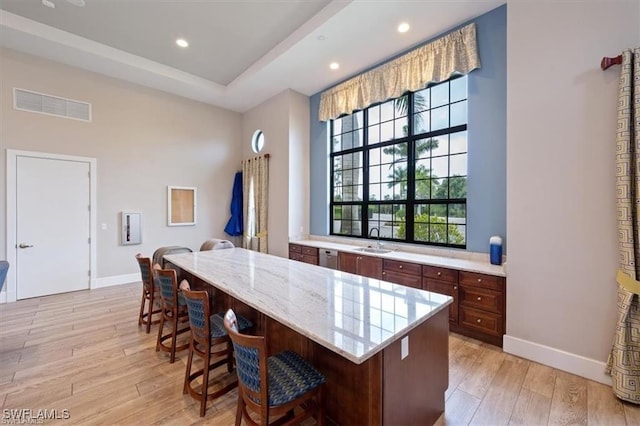 kitchen featuring sink, a kitchen island, light stone countertops, light hardwood / wood-style floors, and a breakfast bar area