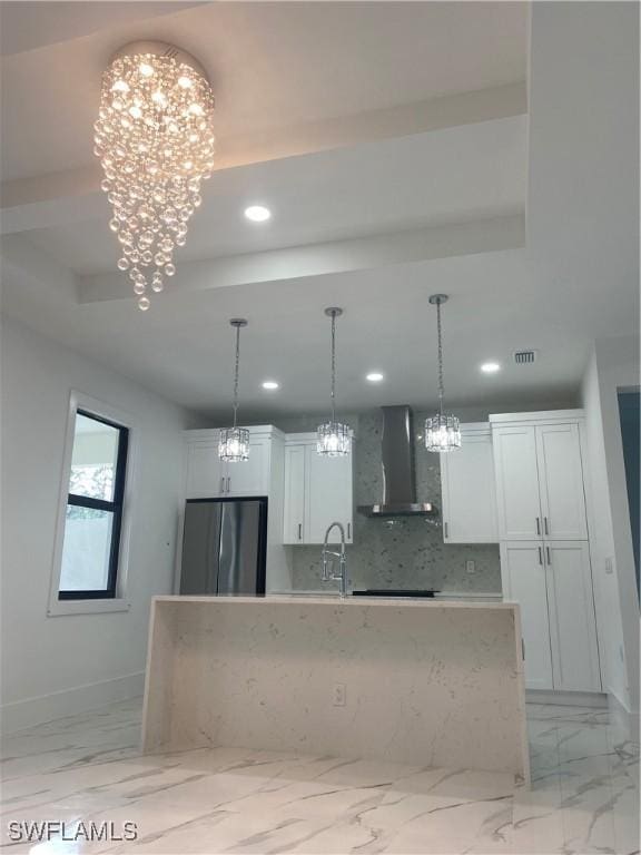 kitchen featuring stainless steel refrigerator, white cabinetry, an inviting chandelier, decorative backsplash, and wall chimney exhaust hood