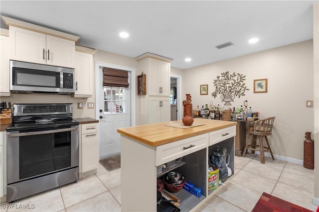 kitchen with butcher block countertops, stainless steel appliances, a center island, and light tile patterned flooring