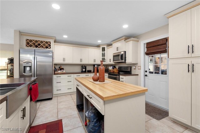 kitchen featuring wood counters, light tile patterned floors, a kitchen island, white cabinetry, and stainless steel appliances