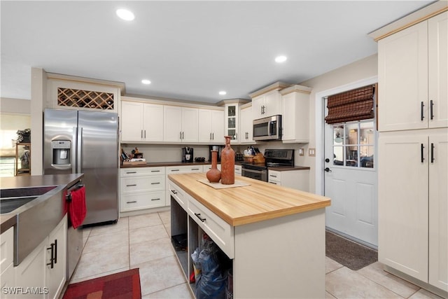 kitchen with stainless steel appliances, a kitchen island, light tile patterned floors, and wood counters