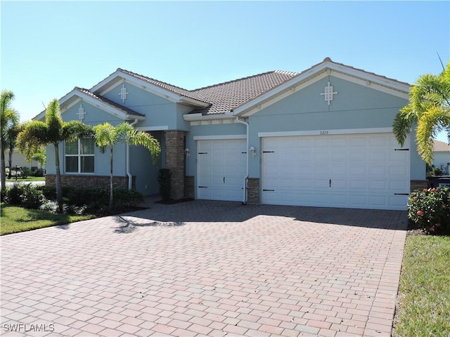 ranch-style home featuring an attached garage, stone siding, a tiled roof, decorative driveway, and stucco siding