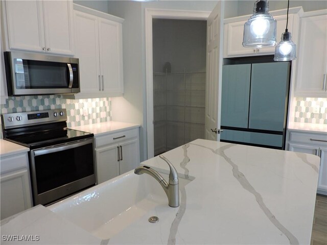 kitchen with decorative backsplash, light stone counters, white cabinetry, and appliances with stainless steel finishes