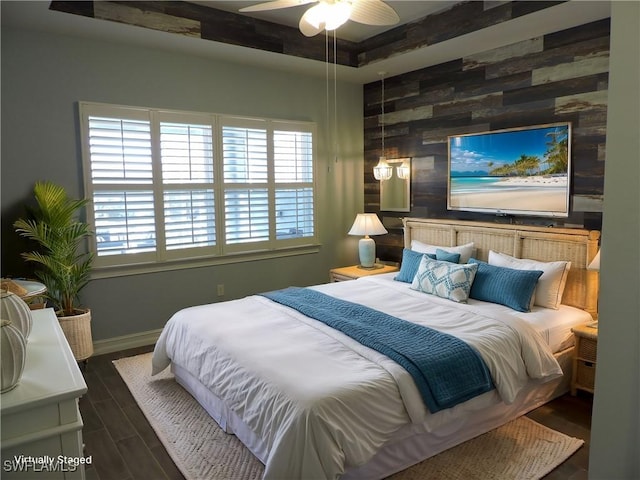 bedroom with a tray ceiling, an accent wall, wooden walls, wood finished floors, and baseboards