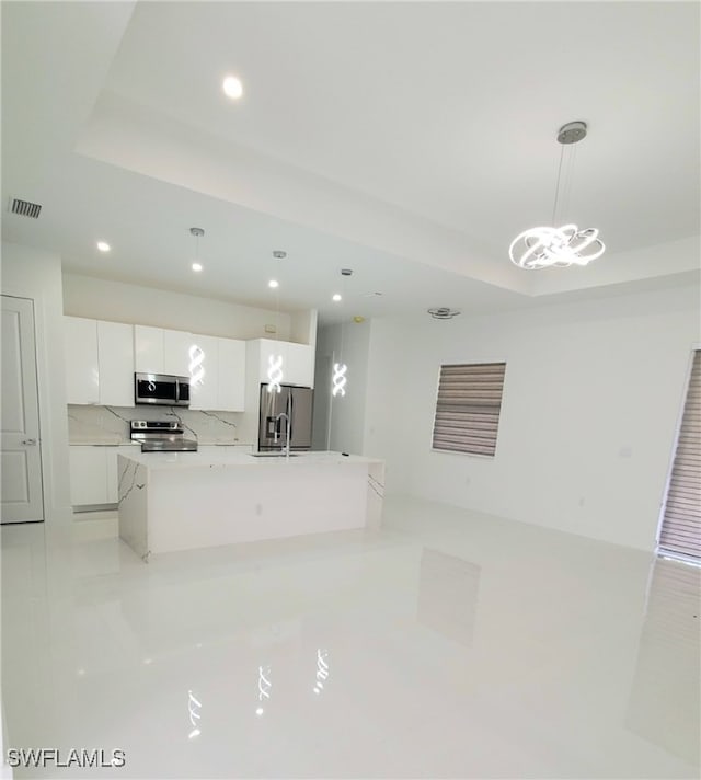 kitchen with appliances with stainless steel finishes, tasteful backsplash, decorative light fixtures, a center island with sink, and white cabinets