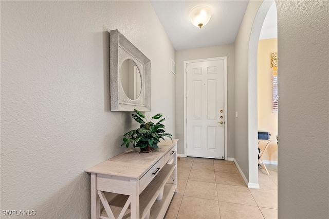 doorway to outside with arched walkways, a textured wall, baseboards, and light tile patterned floors