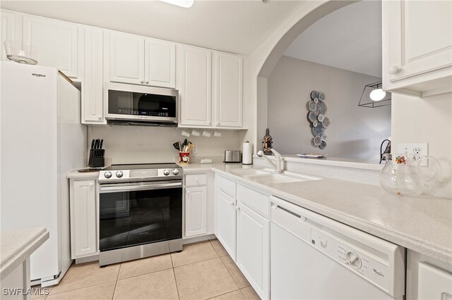 kitchen with light tile patterned flooring, sink, appliances with stainless steel finishes, kitchen peninsula, and white cabinets