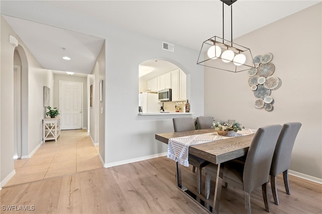 dining area with baseboards, arched walkways, visible vents, and light wood finished floors