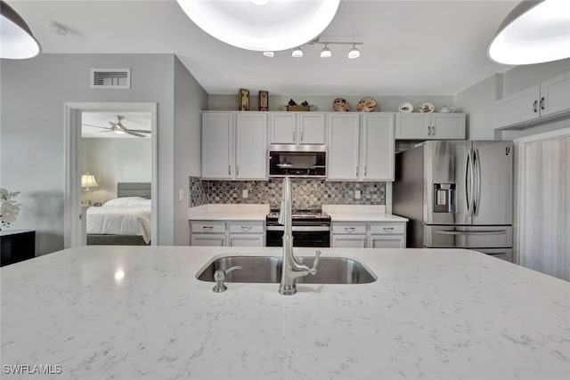 kitchen with sink, ceiling fan, light stone countertops, appliances with stainless steel finishes, and tasteful backsplash