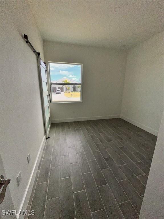 spare room featuring a textured ceiling, a barn door, and dark wood-type flooring