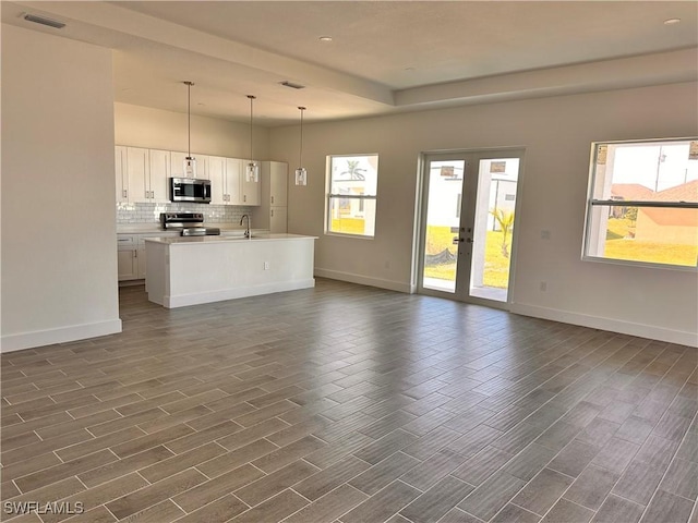 unfurnished living room featuring plenty of natural light, dark hardwood / wood-style flooring, sink, and french doors