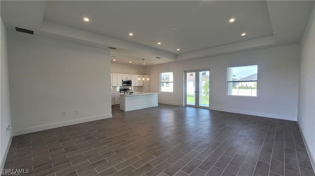 unfurnished living room featuring french doors, dark hardwood / wood-style floors, a tray ceiling, and sink