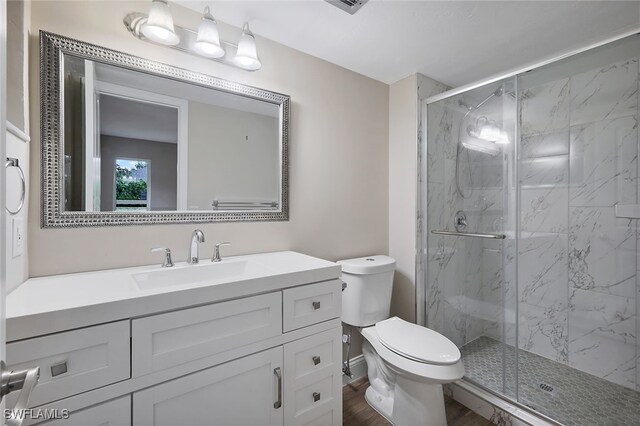 bathroom featuring hardwood / wood-style flooring, a shower with door, vanity, and toilet