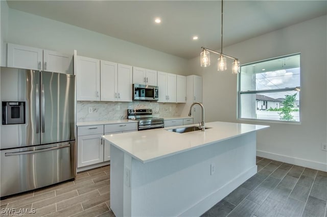 kitchen featuring white cabinetry, sink, stainless steel appliances, decorative light fixtures, and a center island with sink