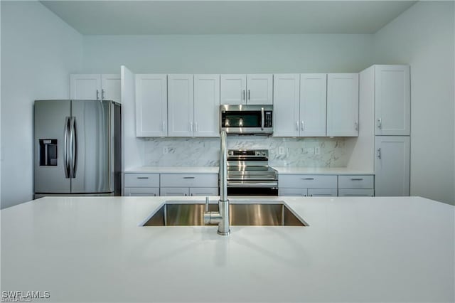 kitchen with tasteful backsplash, sink, white cabinets, and appliances with stainless steel finishes