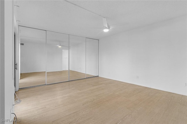 unfurnished bedroom with ceiling fan, a closet, light hardwood / wood-style floors, and a textured ceiling