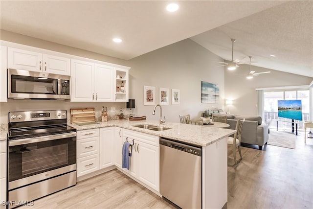 kitchen with kitchen peninsula, stainless steel appliances, sink, white cabinetry, and lofted ceiling