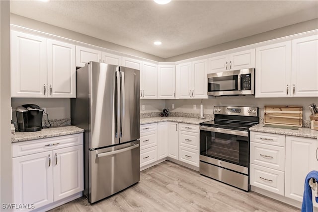 kitchen with light stone countertops, appliances with stainless steel finishes, a textured ceiling, light hardwood / wood-style floors, and white cabinetry