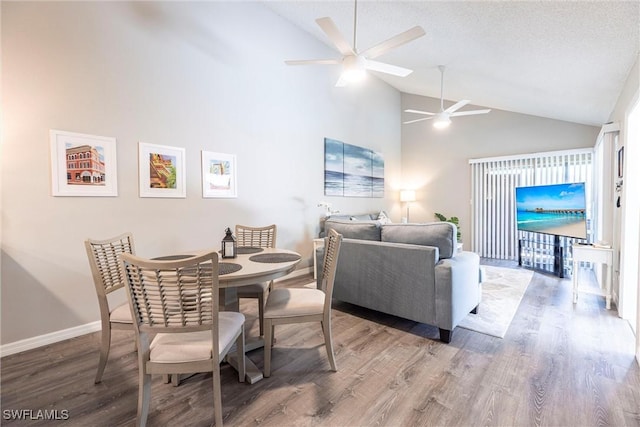 dining area with high vaulted ceiling, a textured ceiling, wood finished floors, baseboards, and ceiling fan