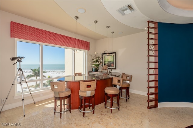 bar featuring a view of the beach, dark stone counters, hanging light fixtures, and a water view