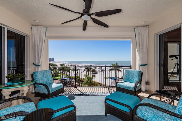 balcony featuring a beach view, ceiling fan, and a water view