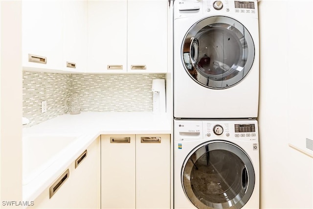 clothes washing area featuring stacked washing maching and dryer and cabinets